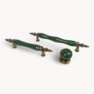 Könnte beinhalten: Ein Set aus vier Schrankbeschlägen: zwei grüne und goldfarbene Stangengriffe und ein grüner und goldfarbener Knauf. Die Beschläge haben eine glänzende grüne Oberfläche und aufwendige goldfarbene Metalldetails. Auf weißem Hintergrund.