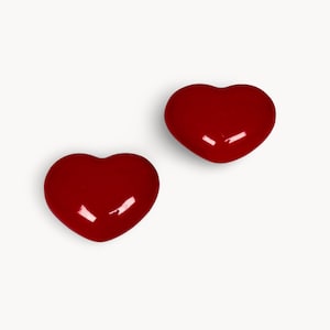 Peut inclure: Deux objets brillants en forme de cœur, d'un rouge vif, sont présentés sur un fond blanc. Les cœurs ont une surface lisse et réfléchissante, suggérant une finition polie. L'image est simple et épurée, les cœurs étant le point central.
