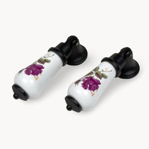 May include: Two white ceramic cabinet pulls with black bases and accents. Each pull features a purple rose design with green leaves. The pulls are designed for easy installation and add a decorative touch.