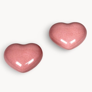 Peut inclure: Deux objets en forme de cœur d'une teinte rose tendre avec un léger scintillement. Les formes lisses et arrondies ont une finition brillante, reflétant la lumière. Les cœurs sont posés sur un fond blanc épuré, soulignant leur forme et leur couleur.