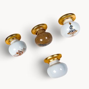 May include: Four decorative cabinet knobs with gold-colored bases. Two knobs are white with floral designs in brown and blue. One knob is brown with blue accents, and the last is white. These knobs are perfect for adding a touch of elegance to any cabinet or drawer.