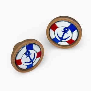 Op de afbeelding: Twee houten kastknoppen met een nautisch thema. Elke knop heeft een wit, rood en blauw ontwerp dat lijkt op een reddingsboei, met een blauw anker in het midden. De knoppen hebben een natuurlijke houten afwerking.