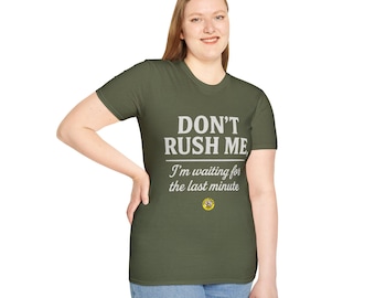 May include: Olive green t-shirt with the text "DON'T RUSH ME" in white block letters. Below, the shirt reads "I'm waiting for the last minute" in a cursive font. A small yellow emblem is at the bottom.