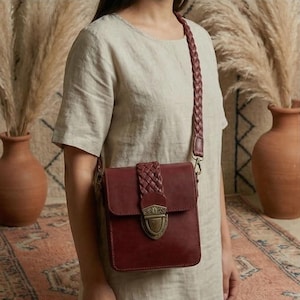 May include: A burgundy leather crossbody bag with a braided strap and flap closure. The bag features a decorative metal clasp and is worn over the shoulder. The bag is rectangular and has a vintage aesthetic.