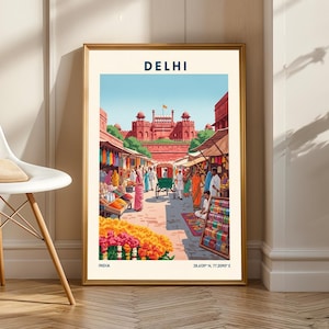 Puede incluir: Impresión enmarcada de Delhi, India, que presenta una bulliciosa escena callejera con un fuerte rojo al fondo. La obra de arte muestra un mercado vibrante con textiles coloridos, flores y personas con vestimenta tradicional. La palabra "DELHI" está en la parte superior.