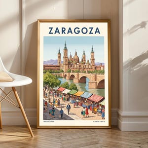 May include: A framed travel poster of Zaragoza, Spain, depicting the Basilica-Cathedral of Our Lady of the Pillar, a bridge, and a vibrant marketplace. The poster is in a gold frame and has the word "ZARAGOZA" in navy blue.