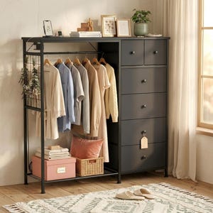 May include: A black metal wardrobe with a clothing rack and drawers. The rack holds various garments on wooden hangers. A pink box, a wicker basket, and a pillow sit on a lower shelf. The top of the wardrobe displays decor and a potted plant.