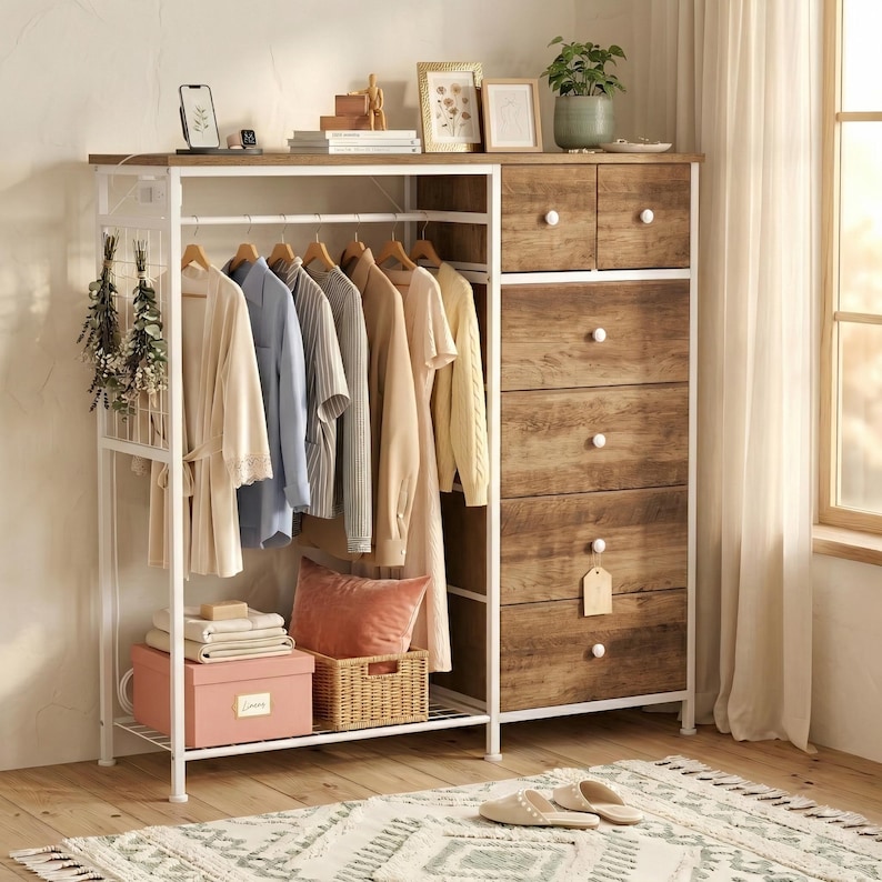 May include: A white metal and wood clothing rack with hanging clothes, a dresser with drawers, and a shelf with decor. The rack holds various garments in neutral colors. The dresser has wooden drawers with white knobs. A rug and slippers are on the floor.