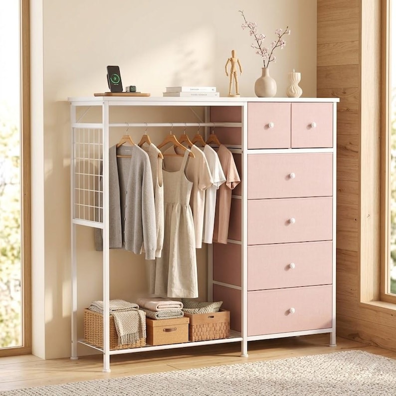 May include: A white metal and pink wardrobe with hanging clothes, drawers, and storage baskets. The wardrobe has a section for hanging clothes, a section with drawers, and a shelf for storage. The drawers are pink with white knobs.