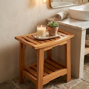 May include: A rectangular wooden stool with a slatted top and a lower shelf. A lit white candle in a glass holder and a small green succulent in a terracotta pot sit on a decorative oval tray placed on the center of the stool's slatted surface.