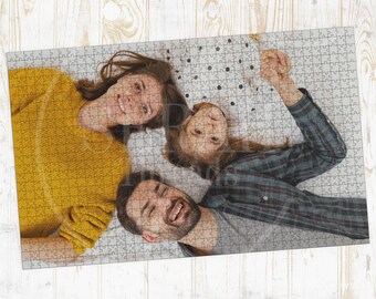 May include: A completed jigsaw puzzle featuring a family portrait. The puzzle shows a smiling woman in a yellow sweater, a young girl, and a man in a plaid shirt. The puzzle pieces are arranged on a light gray surface with a dotted pattern.