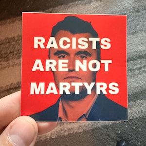 May include: A square sticker with a red background and white text that reads "RACISTS ARE NOT MARTYRS." The sticker features a portrait of a man in a suit.