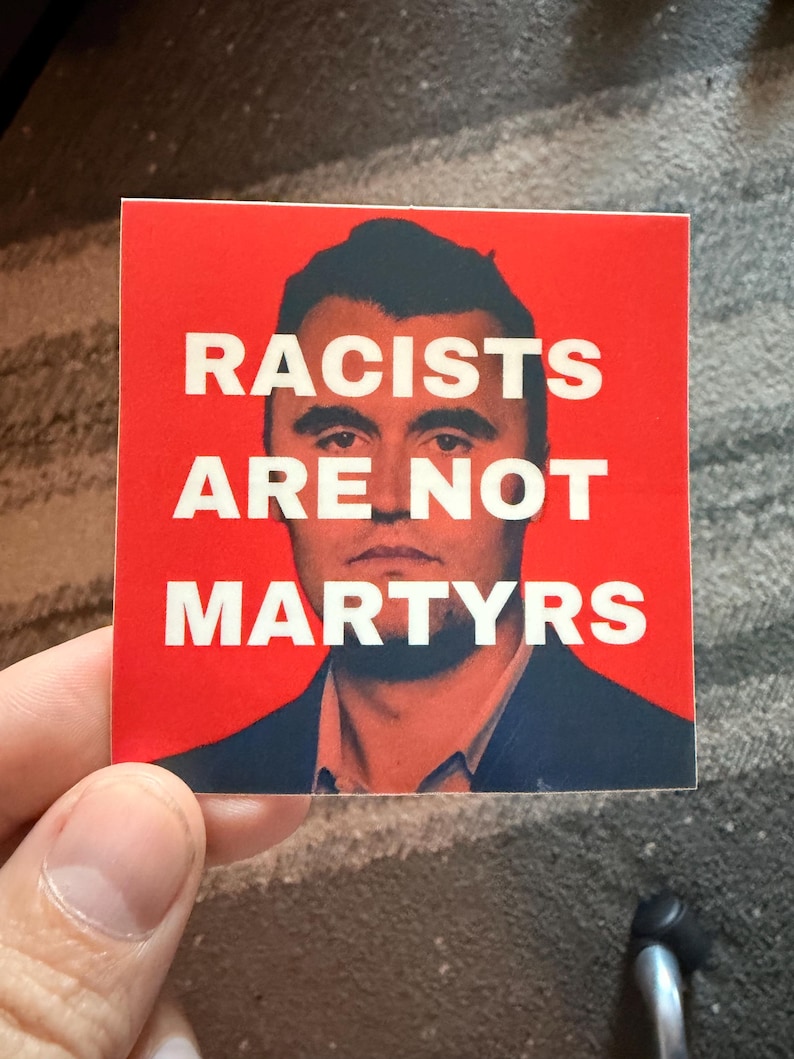 May include: A square sticker with a red background and white text that reads "RACISTS ARE NOT MARTYRS." The sticker features a portrait of a man in a suit.