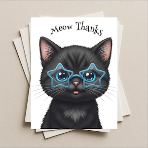 May include: A white greeting card featuring a black cat wearing blue star-shaped glasses. The card has the words "Meow Thanks" in black script above the cat's head. The card is stacked with other white cards.