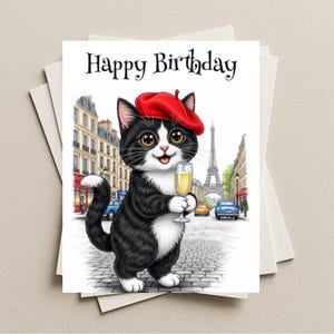 May include: A birthday card featuring a cartoon cat in a red beret holding a champagne glass in front of the Eiffel Tower. The card reads "Happy Birthday" in a black, elegant font. The cat is black and white with yellow eyes.