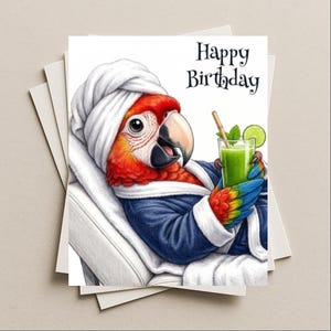 May include: A greeting card featuring a colorful macaw parrot wearing a white towel wrap on its head and a navy blue bathrobe. The parrot holds a green drink with a lime slice and straw. The text Happy Birthday is printed in black at the top right.