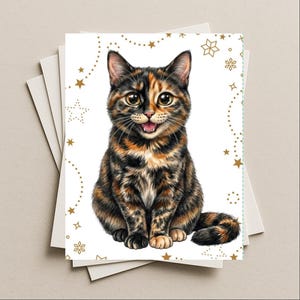 May include: A greeting card featuring a detailed illustration of a tortoiseshell cat with large eyes and an open mouth. The cat has black, orange, and brown fur. The white background is decorated with gold-colored stars and snowflake patterns.