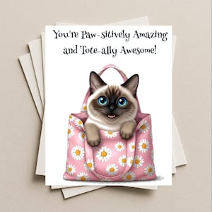 May include: Greeting card featuring a Siamese cat peeking out of a pink tote bag decorated with white daisies. The card reads "You're Paw-sitively Amazing and Tote-ally Awesome!" on a white background. Several blank cards are visible behind the main card.
