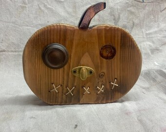 May include: Wooden pumpkin decoration with a stem and metal accents. The pumpkin has a stitched mouth and a brass nose. The eyes are made of metal and the pumpkin is made of wood.