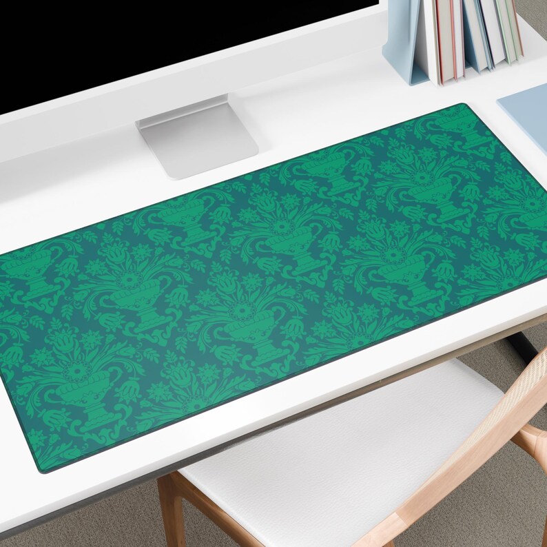 May include: A rectangular desk mat featuring a teal background and a repeating green floral pattern. The design includes stylized vases and foliage. The mat is on a white desk, with a computer monitor and other office supplies.