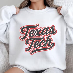 May include: White sweatshirt with the words "Texas Tech" in a black, red, and white design. The text is in a cursive font. The sweatshirt is a crew neck style.