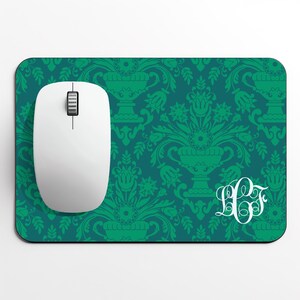May include: A white computer mouse sits on a teal mouse mat with a green floral damask pattern. The mouse mat features a white monogram in the lower right corner. The mouse has a scroll wheel and two buttons.