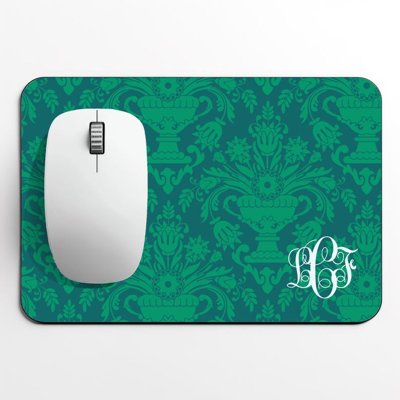 May include: A white computer mouse sits on a teal mouse mat with a green floral damask pattern. The mouse mat features a white monogram in the lower right corner. The mouse has a scroll wheel and two buttons.