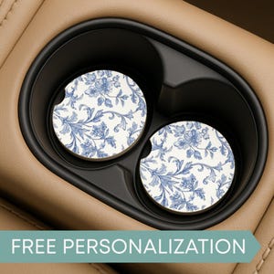 May include: Two round car coasters with a blue floral design on a white background. The coasters are placed in a black car cup holder. The text "FREE PERSONALIZATION" is at the bottom of the image.