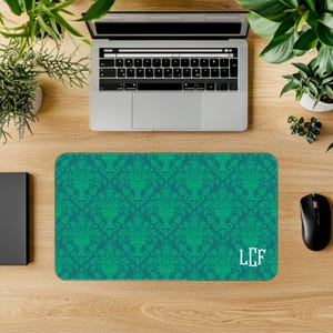 May include: A rectangular teal and green mouse mat featuring a damask pattern and the initials "LCF" in white. The mouse mat is on a wooden desk with a laptop, mouse, and plants.