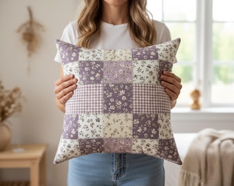 May include: A square throw pillow featuring a patchwork design of alternating fabric squares. The pattern consists of light purple and cream floral prints mixed with a small-scale purple and white gingham check, creating a grid-like aesthetic.