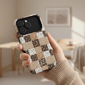 Puede incluir: Una funda de teléfono con un diseño de patchwork en tonos marrones, beige y blanco. La funda presenta una mezcla de patrones florales y a cuadros, creando un efecto acolchado. La funda tiene un módulo de cámara negro y un pequeño emblema decorativo.