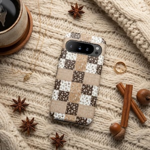 May include: A phone case with a patchwork design in shades of brown, beige, and white, resting on a cream-colored cable-knit sweater. Accompanying the phone are star anise, a gold ring, a cup of coffee, and cinnamon sticks.