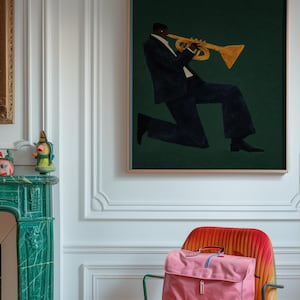 May include: An art print shows a musician playing a trumpet against a dark green backdrop. A pink satchel bag and a smaller pink handbag are on a colourful chair. The room has white walls and a green fireplace.