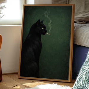 May include: A framed art print featuring a black cat with yellow eyes, smoking a cigarette. The cat is set against a dark green background. The artwork is displayed in a light wood frame, leaning against a wall.