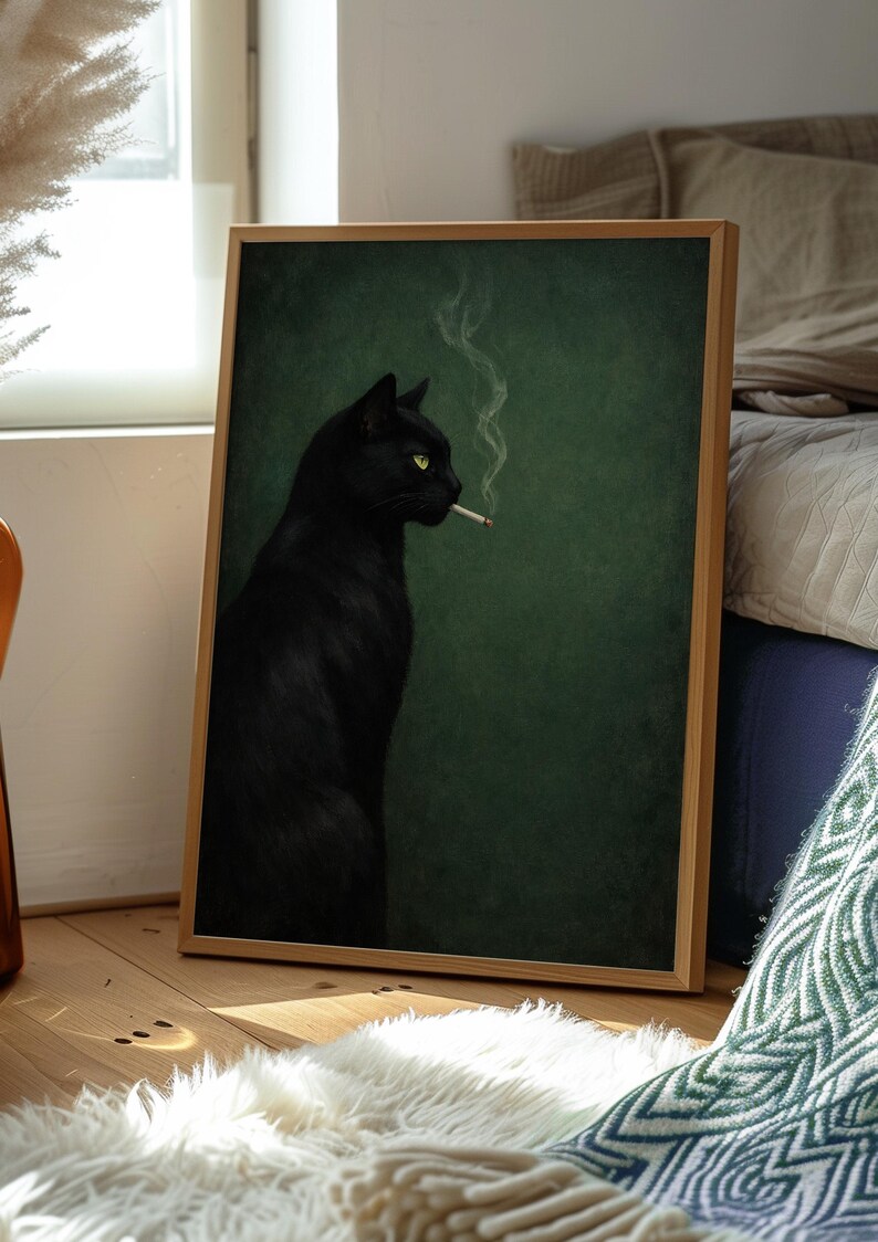 May include: A framed art print featuring a black cat with yellow eyes, smoking a cigarette. The cat is set against a dark green background. The artwork is displayed in a light wood frame, leaning against a wall.