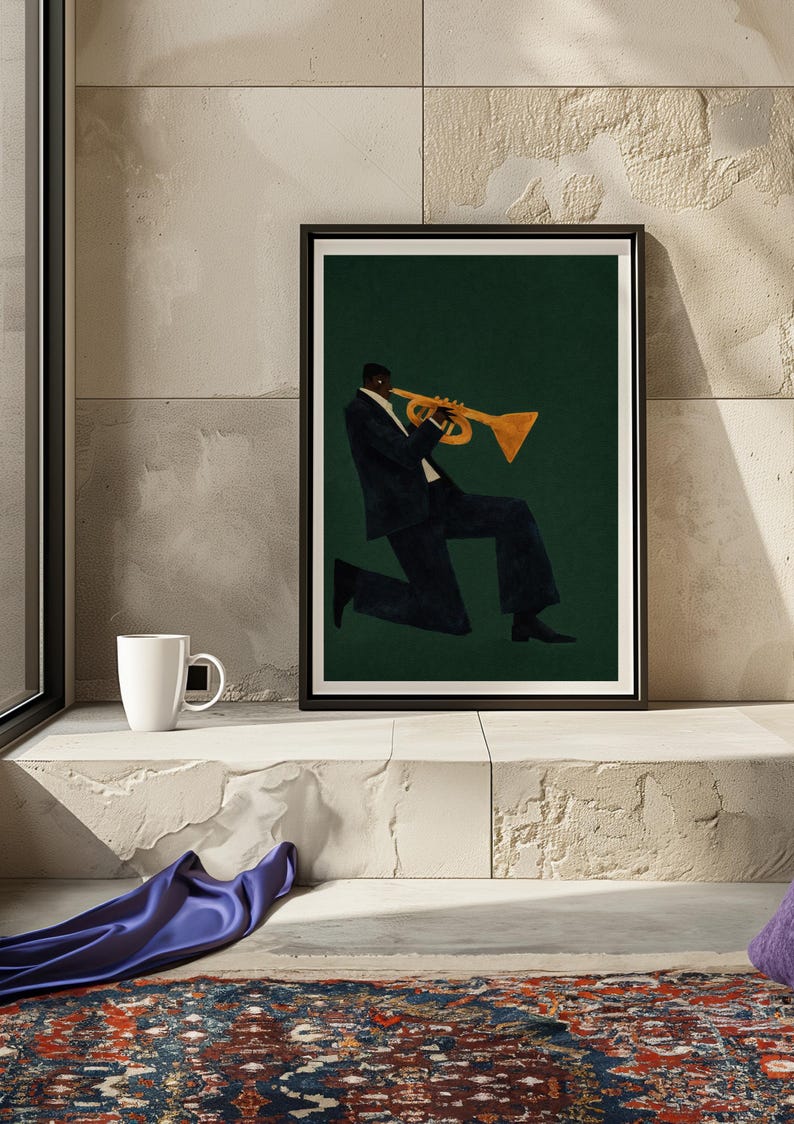 May include: Framed art print showing a musician playing a trumpet. The artwork depicts a person in a dark suit against a dark green background. The trumpet is gold-coloured. The print is displayed on a white ledge, with a white mug.