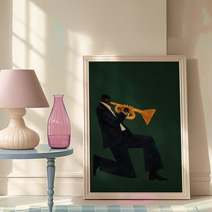 May include: Framed art print of a musician playing a trumpet. The artwork shows a person in a dark suit and white shirt, playing a gold trumpet against a dark green background. The print is in a silver frame.