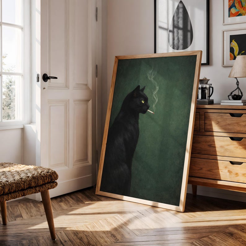 May include: A framed art print featuring a black cat with yellow eyes smoking a cigarette. The cat is set against a dark green background, with smoke rising from the cigarette. The artwork is displayed in a room with wooden furniture and a natural light.