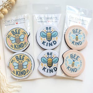 May include: Car coasters with a bee and floral design. The coasters have the words "BEE KIND" and "BE KIND" printed on them. The coasters are packaged in clear plastic.