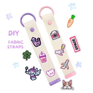 Peut inclure: Deux lanières en tissu blanc cassé avec des écussons brodés colorés, dont un appareil photo, un château et un chien. Les lanières ont des accents violets et roses et des anneaux métalliques. Le texte "DIY FABRIC STRAPS" est visible.