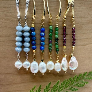 May include: A collection of handmade earrings with various gemstone and pearl designs. The earrings feature blue, green, and red gemstones, along with white pearls. The metal components are gold and silver.