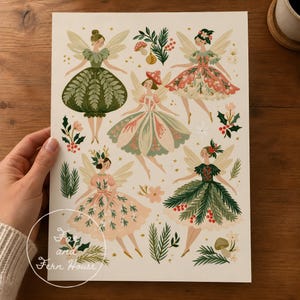 Op de afbeelding: Een kunstdruk met vijf geïllustreerde feeën met vleugels, gekleed in jurken geïnspireerd op botanische elementen zoals varenbladeren, dennentakken en bloemen. Het ontwerp bevat kleine paddenstoelen, hulstbessen en de tekst Fae and Fern House.