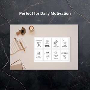 Puede incluir: Una tarjeta rectangular blanca con ocho frases motivacionales e iconos, incluyendo "Me comunico claramente" y "Elijo pensamientos positivos". La tarjeta est&aacute; sobre una superficie beige claro con una vela, bol&iacute;grafos y un bloc de notas.