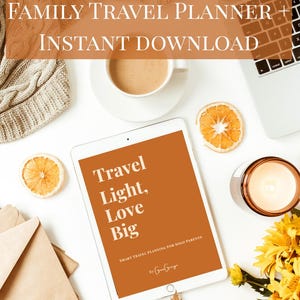 May include: A tablet shows the words "Travel Light, Love Big" on an orange screen. The image includes a coffee cup, dried orange slices, a laptop, a candle, and flowers, suggesting a travel planning theme.