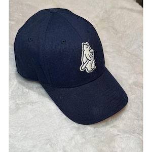 May include: A navy blue baseball cap with a curved brim. The cap features a white embroidered bear logo holding a baseball bat on the front. The cap is made of a durable fabric and has a structured fit.