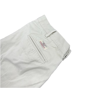 May include: Pale beige trousers with a back pocket and a label reading "CLASSIC FIT POLO". The trousers are folded, suggesting they are new. The style is casual and suitable for everyday wear.