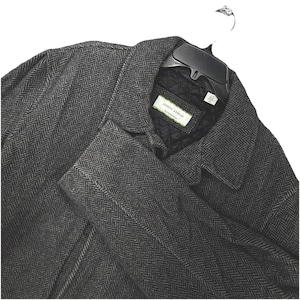 May include: A dark grey herringbone pattern coat by Joseph Abboud. The coat is hanging on a black hanger. The coat has a notched collar and a quilted lining. The label reads "JOSEPH ABBOUD OUTERWEAR".