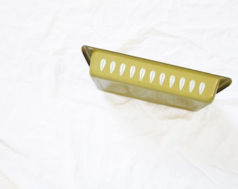 Könnte beinhalten: Eine gelbe Emaille-Backform mit einem weißen Blattdesign. Die Form ist leer und steht auf einer weißen Oberfläche.