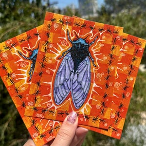 Può includere: Una stampa artistica rettangolare con un'illustrazione centrale di una cicala blu e nera circondata da un bagliore bianco. Lo sfondo è costituito da un motivo a scacchi arancione e giallo bordato da una cornice di piccole formiche nere e spirali.