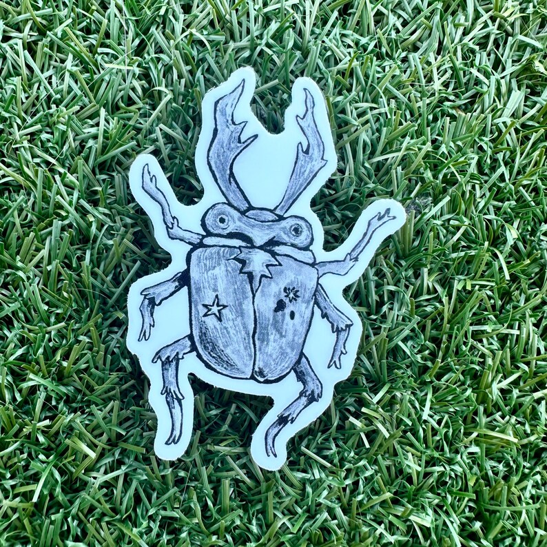 May include: A sticker featuring a detailed illustration of a beetle with large antlers and six legs. The beetle is drawn in black and white with a star and floral design on its back. The sticker is on a white background.